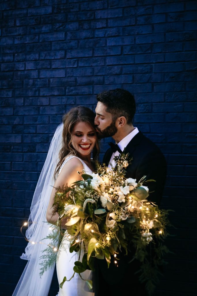 The groom kisses his bride with a bouquet with a light feature.