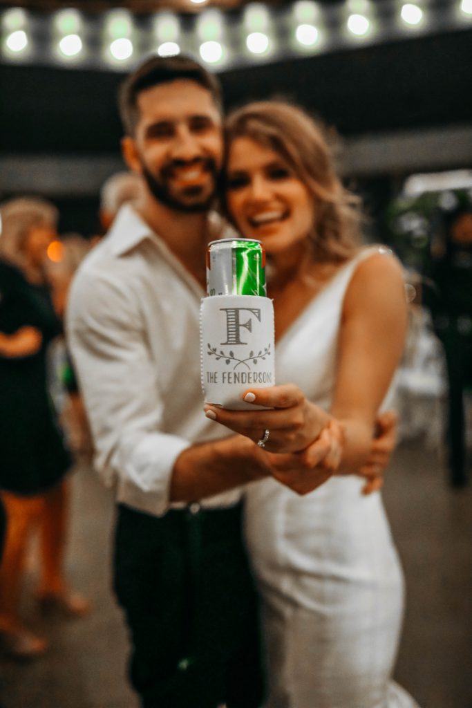 bride and groom holding a fun wedding koozie with their new last name.