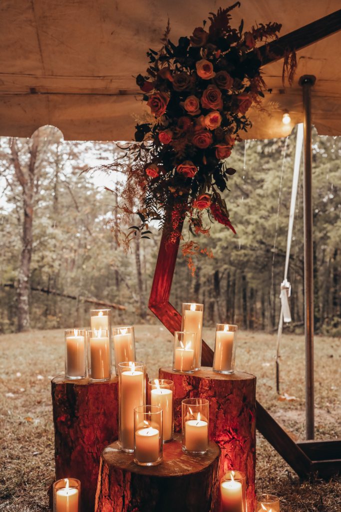 Glam flowers on a boho arbor with pillar candles glowing under a tent for a wedding.