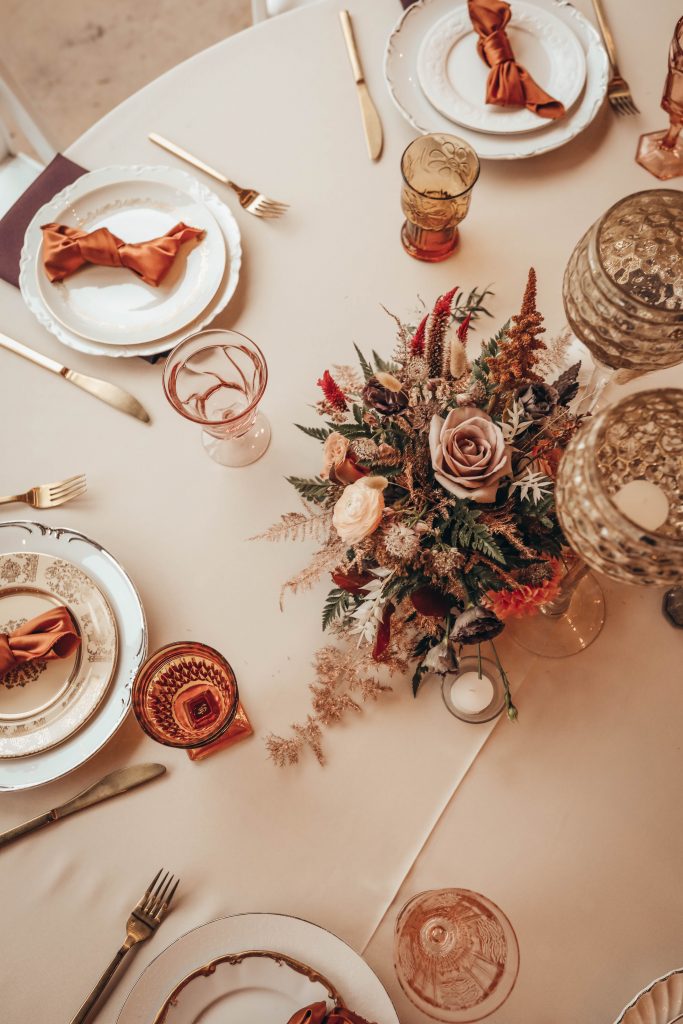 Boho glam wedding tablescape featuring assorted vintage china and burnt orange silk napkin with amazing flowers.