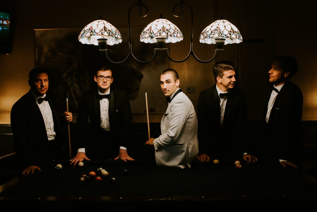 The groom and his men post for a picture around a pool table.