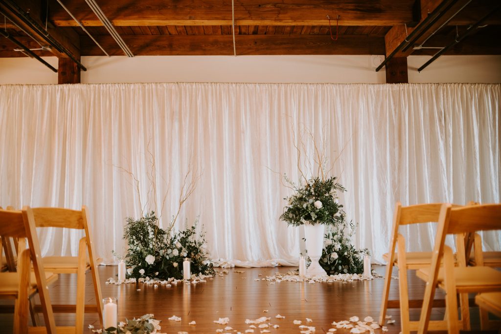Beautiful white draping with greenery and candles made a perfect backdrop for the altar for this industrial chic wedding.